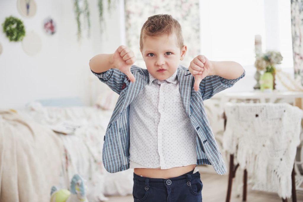 A young boy in a blue suit showing a thumbs-down, symbolizing how children are often mislabeled as “bad kids” when they are actually seeking connection.