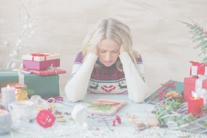 A stressed woman sitting at a holiday table surrounded by gifts, wrapping supplies, and Christmas decorations, symbolizing holiday overwhelm and the need for a calmer, stress-free season.