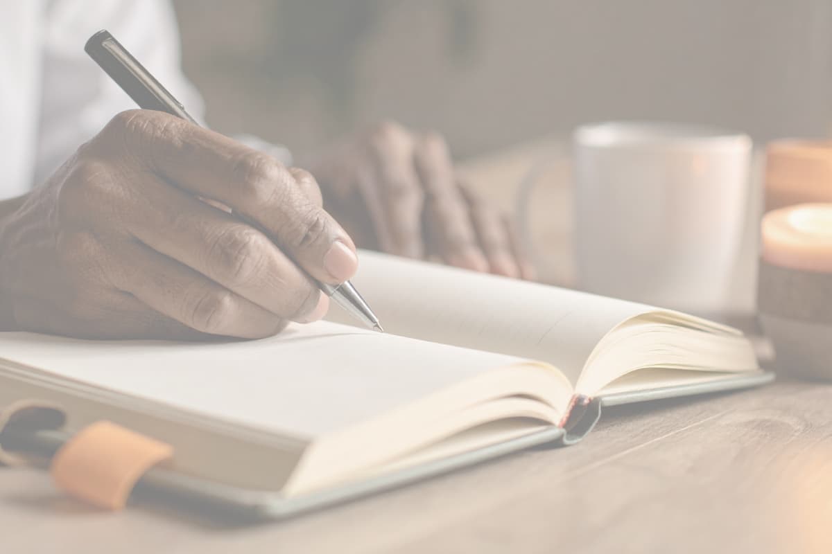 Close-up of a person writing in a blank journal with a pen on a cozy wooden table, symbolizing intentional goal setting and reflection