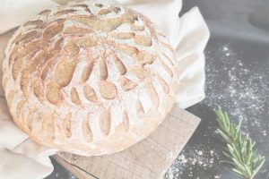 Freshly baked sourdough bread on a wooden board with flour dust and rosemary, symbolizing growth, patience, and mindful living.