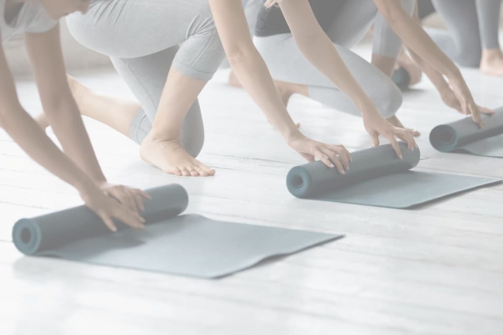 Participants preparing for a Pilates class by rolling out yoga mats in a bright studio, representing emotional compensation, self-awareness, and healing.