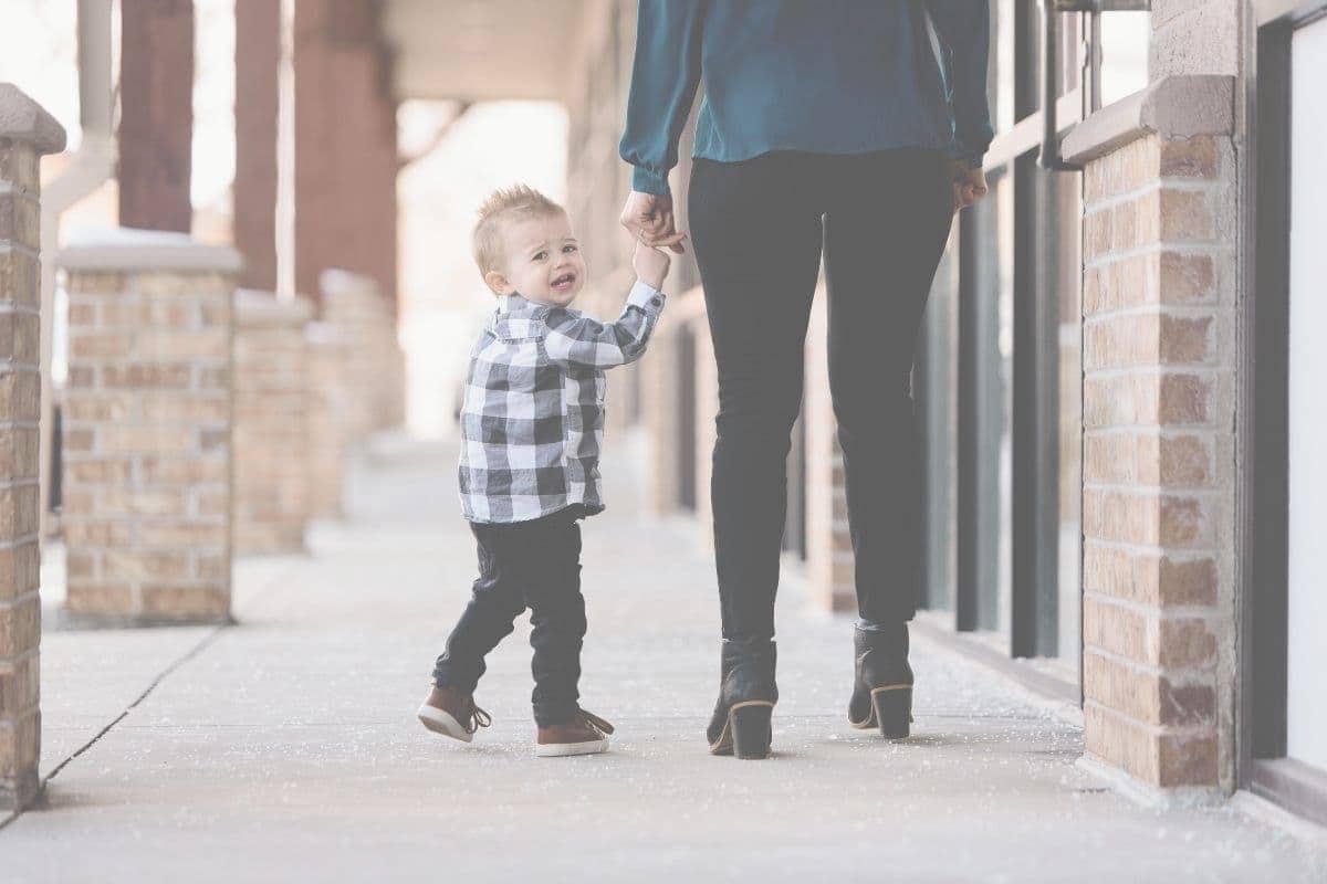 Toddler holding mother’s hand while looking upset, showing emotional connection and co-regulation in conscious parenting