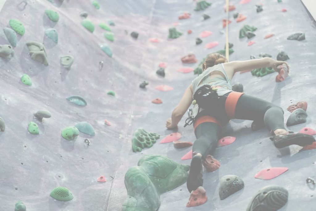 A woman is indoor rock climbing while overcoming fear and learning to trust the belay system, symbolizing letting go of control and trusting life's journey.