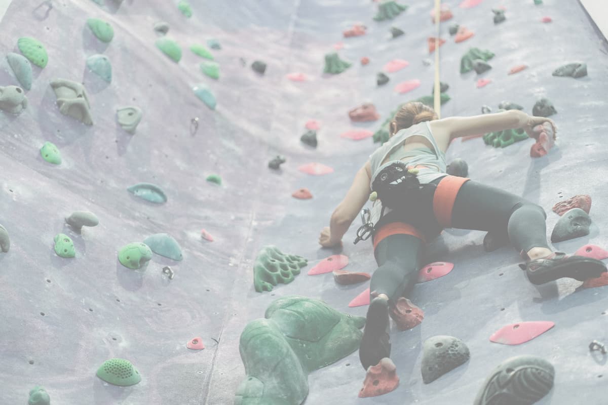 A woman is indoor rock climbing while overcoming fear and learning to trust the belay system, symbolizing letting go of control and trusting life's journey.