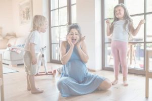 Overwhelmed mother sitting on the floor between two upset children during a family meltdown, illustrating power struggles with toddlers and conscious parenting challenges.
