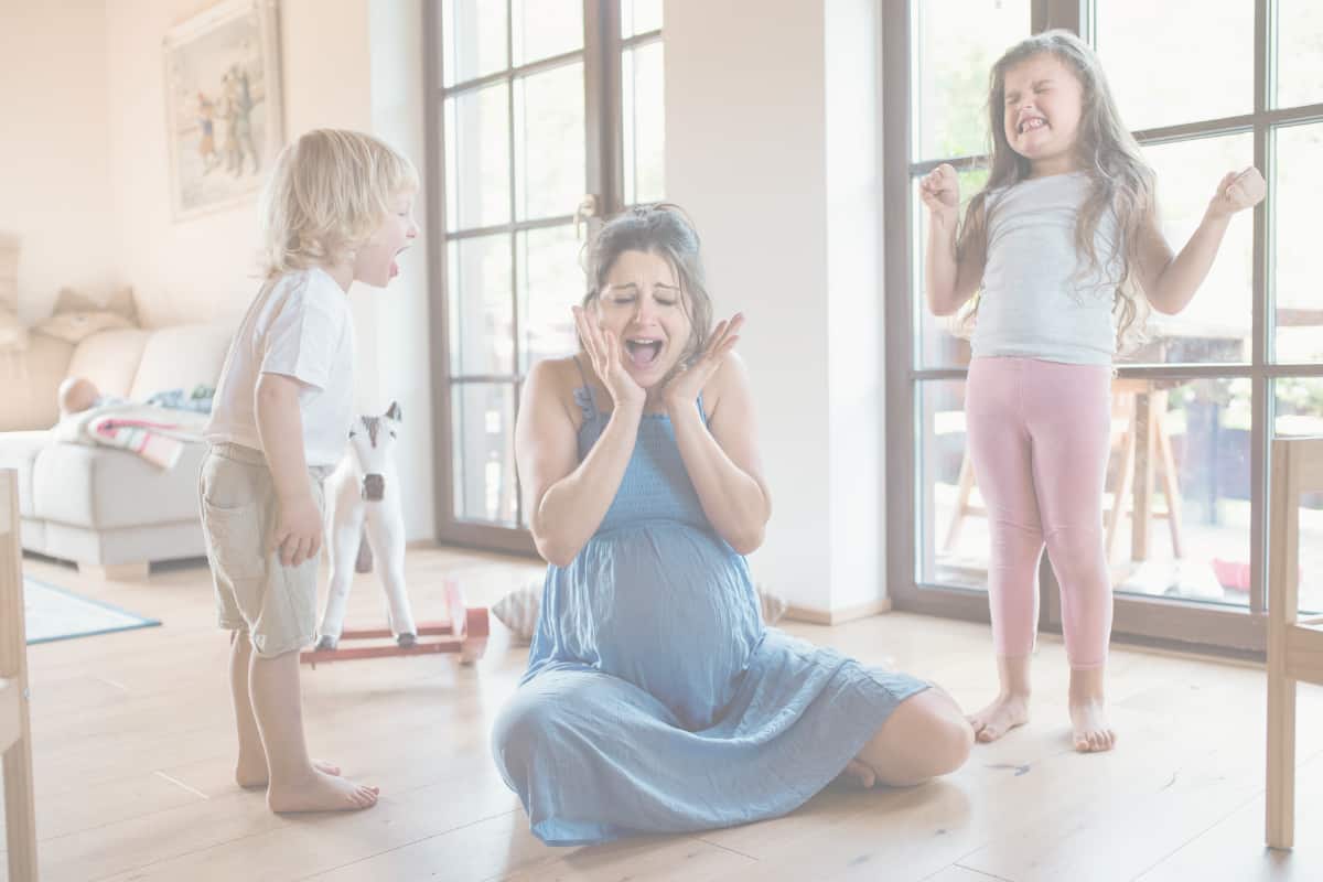 Overwhelmed mother sitting on the floor between two upset children during a family meltdown, illustrating power struggles with toddlers and conscious parenting challenges.